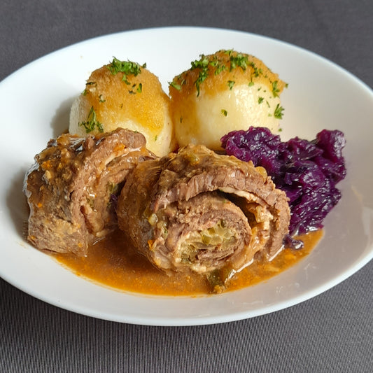 Rinderroulade auf einem Teller, angerichtet mit Rotkraut und Kartoffelkloeßen als Serviervorschlag