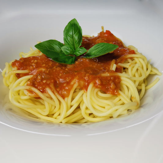 hausgemachte Sauce Bolognese auf Nudeln auf einem Teller, angerichtet mit frischem Basilikum als Serviervorschlag