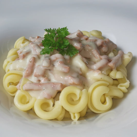 Pasta mit Sauce Carbonara mit Schinken auf Trullinudeln, auf einem Teller garniert mit Petersilie
