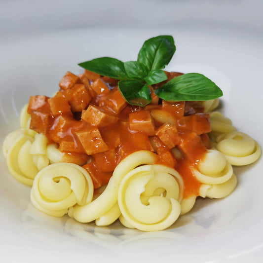 hausgemachte Tomatensauce mit Wurstgulasch auf Nudeln angerichtet auf einem Teller als Serviervorschlag, garniert mit frischem Basilikum