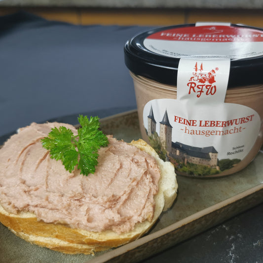 Brotscheibe mit cremiger aufgestrichener hausgemachter Leberwurst, garniert mit frischer Petersilie, neben der Glaskonserve